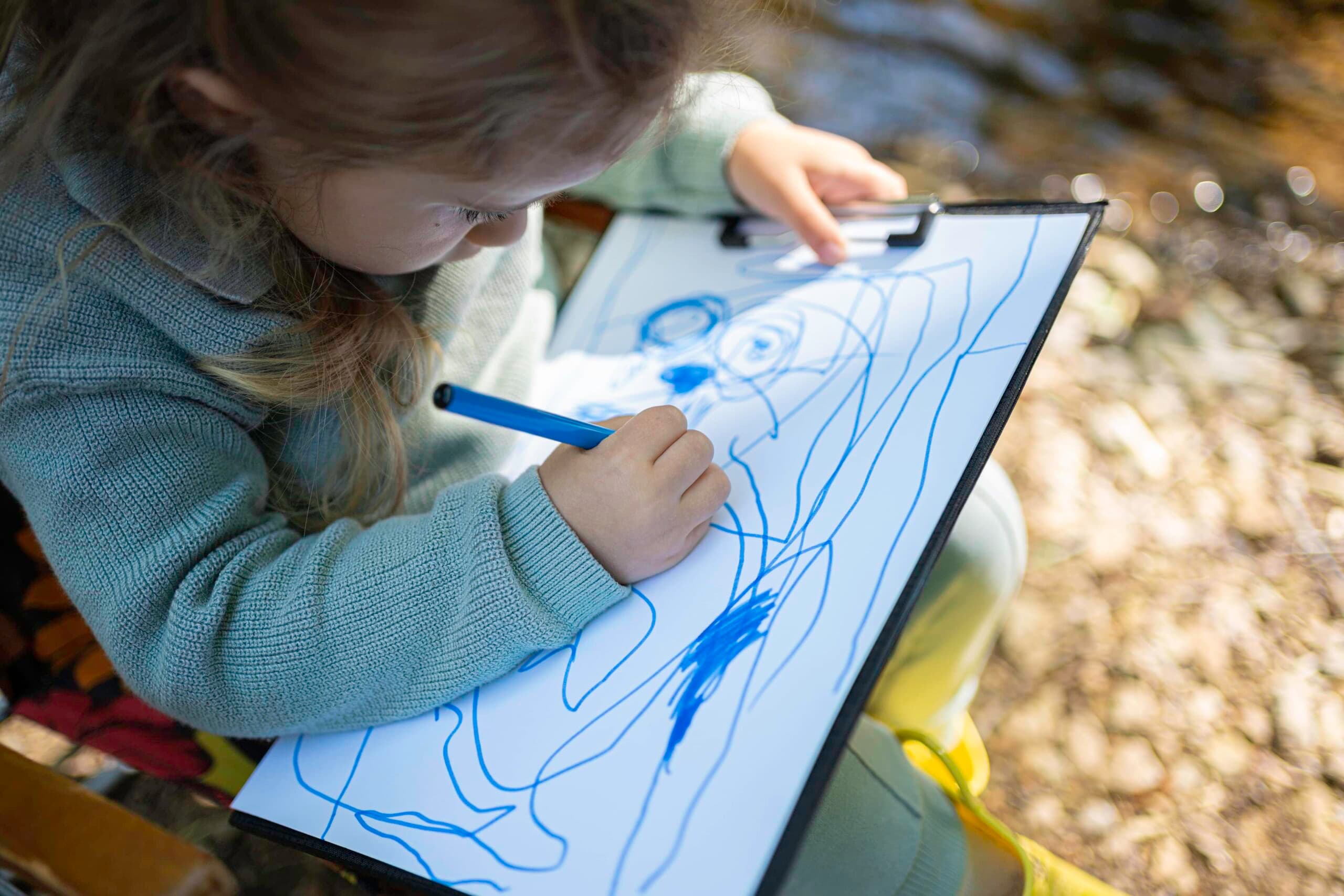 Child holding a marker and clipboard, drawing