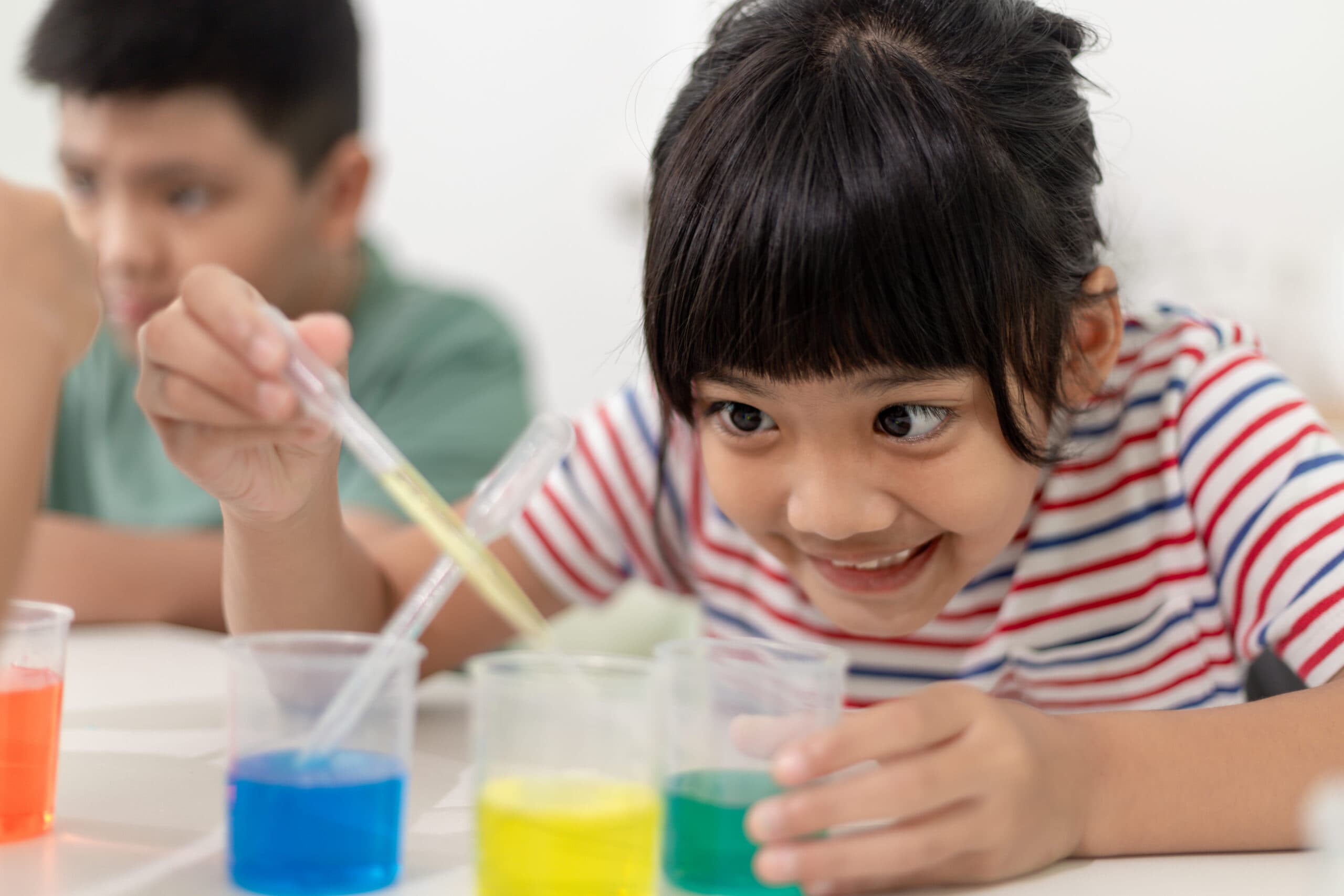 child uses pipette to squeeze colorful paint from cups